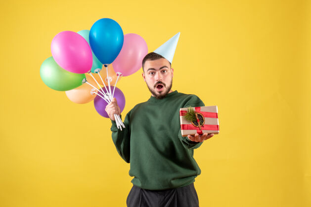背景正面图：手持彩色气球的年轻男性 呈现在黄色背景上聚会礼物年轻男性
