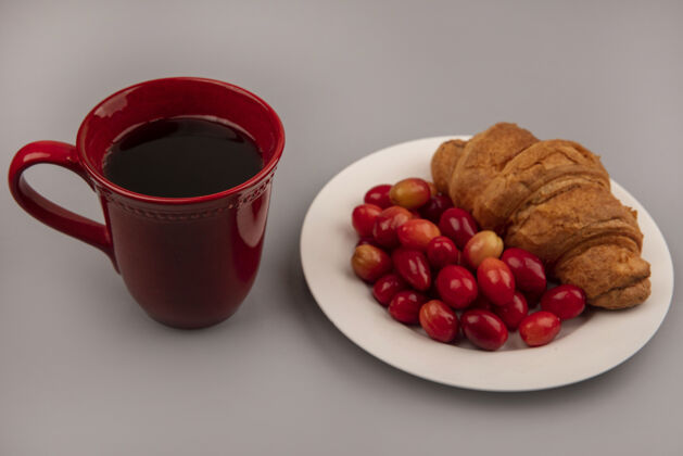 酸的白色盘子上夹着牛角面包 灰色墙壁上放着一杯咖啡 酸甜的山茱萸樱桃的俯视图盘子咖啡风景