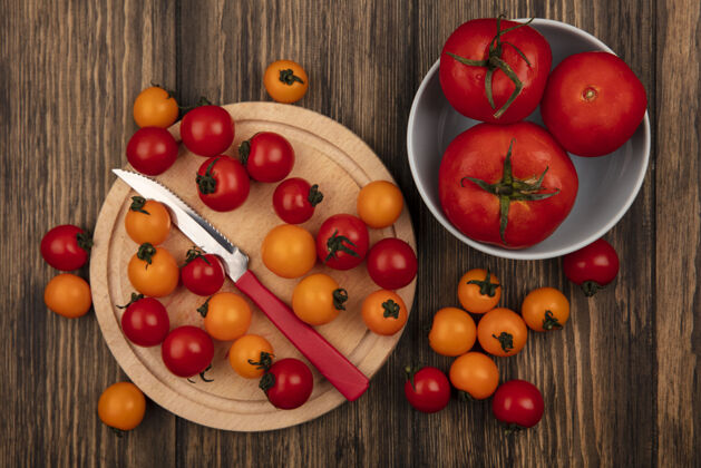 板顶视图新鲜的红色和橙色樱桃西红柿隔离在一个木制的厨房板与大尺寸的西红柿在一个碗在一个木制的墙壁刀大小碗新鲜