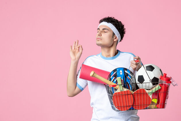 篮子正面图穿着运动服的年轻男子 带着装满运动用品的篮子 粉色的墙壁好购物景观
