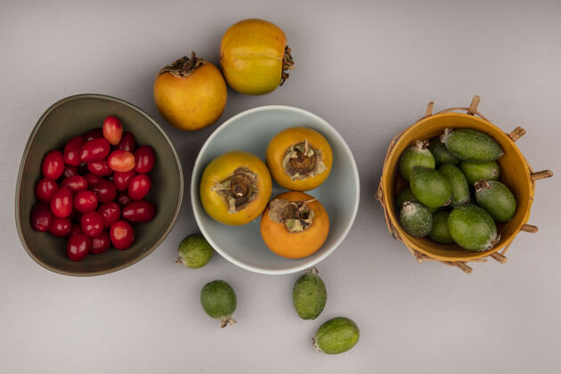 午餐橘子柿子水果放在碗里的顶视图 桶上有飞珠 灰色墙壁上的碗上有山茱萸樱桃甜点食物水果