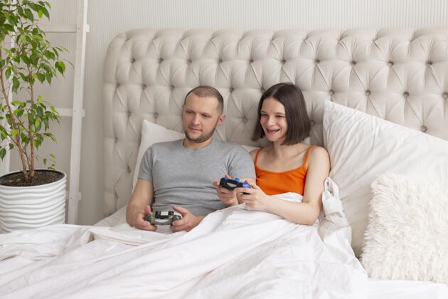 玩家夫妻俩在床上玩电子游戏享受操纵杆游戏