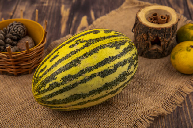哈密瓜新鲜的哈密瓜在布袋上的顶视图 肉桂棒和松果放在木桶上的木墙上火腿瓜锥