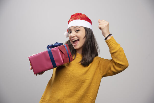圣诞老人戴着圣诞帽的黑发女人伸出拳头 手里拿着礼盒漂亮女人女孩