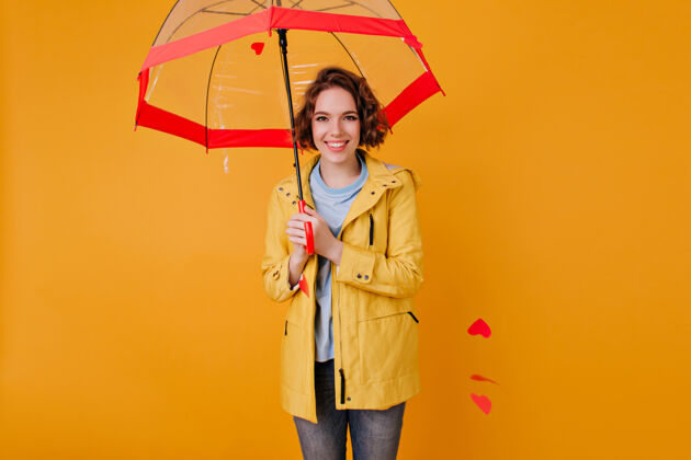 季节黄色墙壁上高加索女孩手持红色阳伞 面带微笑室内照片 优雅的年轻女子 卷发 站在伞下漂亮表情情绪