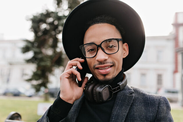 积极黑眼睛的非洲男子在电话交谈中摆姿势情绪激动的黑人男子拿着智能手机坐在公园里的户外特写照片设备混血儿电话