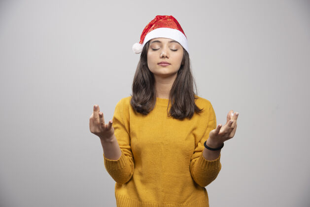 女人戴圣诞帽的女人在灰墙上冥想年轻女性圣诞老人