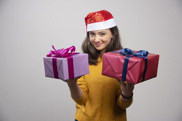 女孩戴着圣诞老人红帽子的年轻女子 手里拿着圣诞礼物礼品盒帽子女士