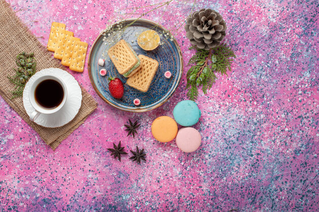 化妆品俯瞰美味的华夫饼 在粉红色的表面上放上一杯茶和麦卡龙饼干生的洗漱用品
