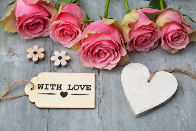 开花粉红色玫瑰的特写镜头 旁边是一个空心木标签和一个木制表面上的怀有爱标签信息开花木