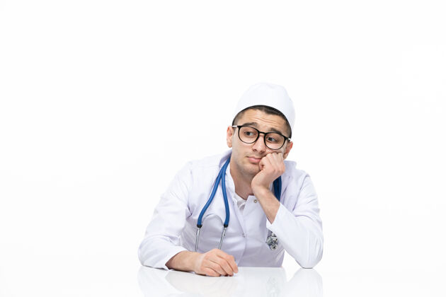 药品正面图：坐在书桌后面的男医生穿着医疗服专业医生听诊器