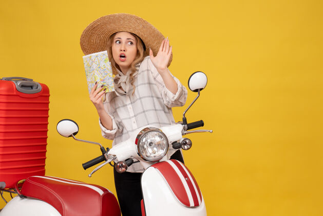 摩托车俯视图：一个戴着帽子的年轻女子坐在摩托车上拿着地图 正在收行李顶年轻女子坐