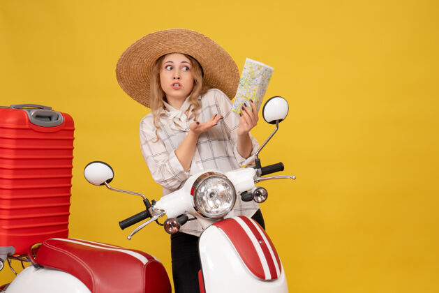地图俯视图：好奇的年轻女子戴着帽子坐在摩托车上拿着地图收行李收集帽子顶