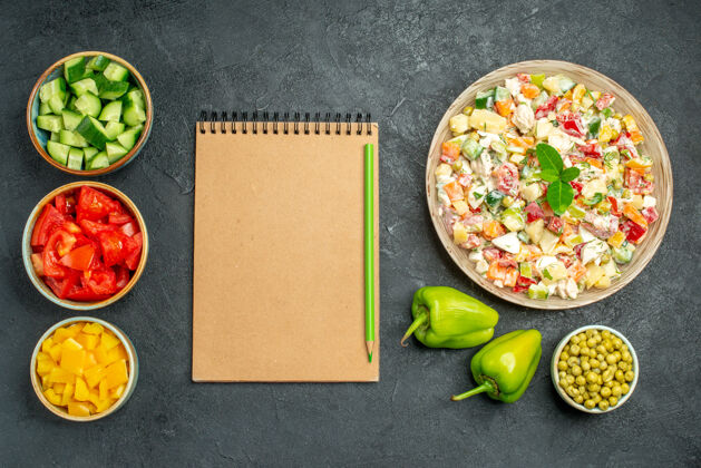 胡椒粉一碗蔬菜沙拉的俯视图 深绿色桌子上有一碗蔬菜记事本和甜椒碗餐厅壁板