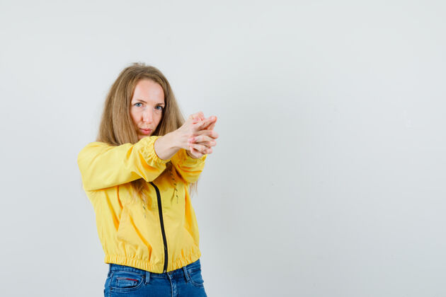 时尚身穿黄色棒球服和蓝色牛仔裤的年轻女子 展示着持枪的姿势 看上去很乐观 正前方的景色肖像年轻漂亮