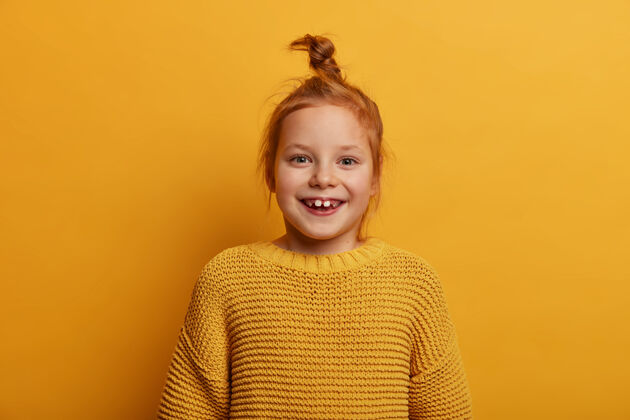 满意快乐可爱的孩子 自然的姜黄色头发 微笑积极 看起来积极的心情 穿着针织黄色毛衣 注意到一些不可思议的和吸引人的东西 笑得牙牙学语发髻姜毛衣