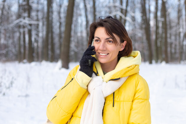 雪心情愉快的快乐女人漫步在雪域的冬日森林里 愉快地聊着电话 享受着公园里的户外时光站女性雪景