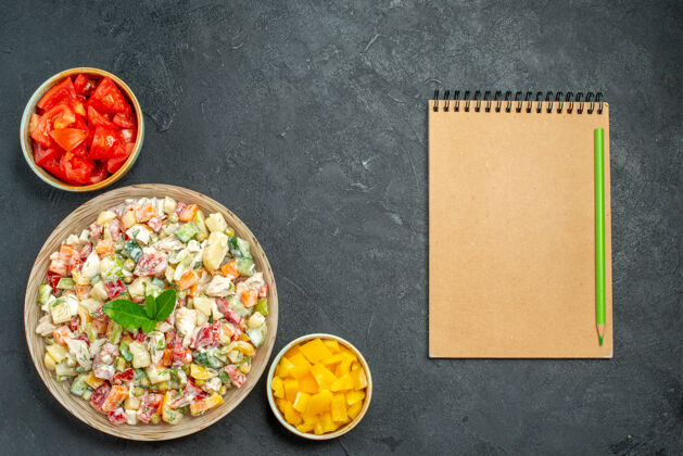 美味蔬菜沙拉碗的俯视图在左下角 蔬菜碗和记事本在深绿色的灰色背景上背景饮食记事本