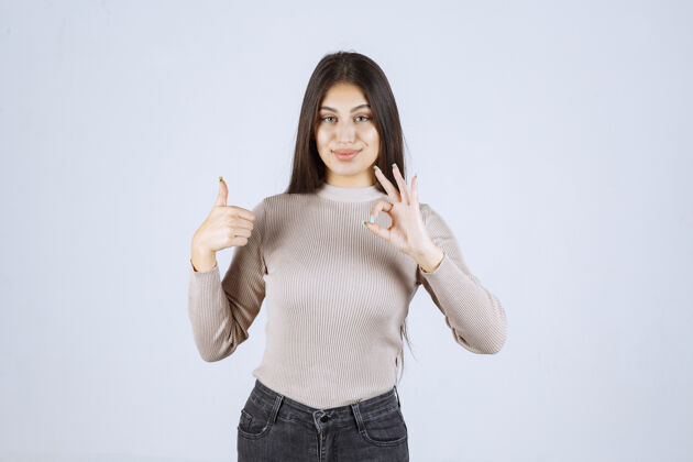 人类穿灰色衬衫的女孩在做竖起拇指的招牌协议女人积极