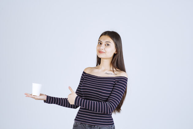 工人穿着条纹衬衫的女孩拿着一个塑料咖啡杯 指着一个好味道聪明雇员人体模特