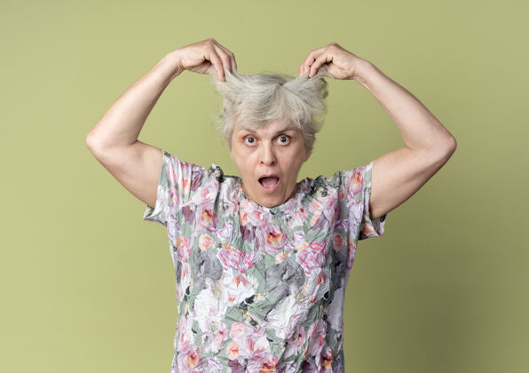 老年人震惊的老妇人抬起橄榄绿墙上孤立的头发女人老年人举起来