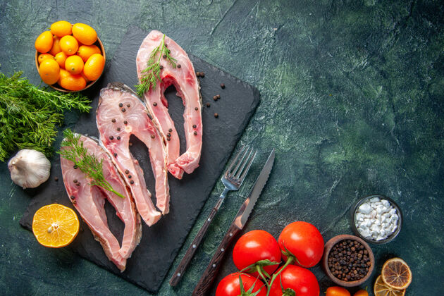 食物顶视图新鲜鱼片与绿色红色西红柿和金橘在黑暗的背景深色晚餐肉类
