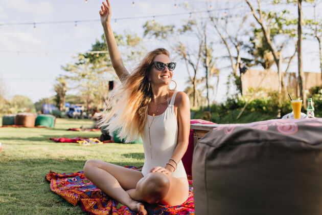 阳光穿着泳衣的浅棕色女人坐在草坪上挥手一个金发碧眼的可爱年轻女人在公园里玩的户外写真健康放松女性