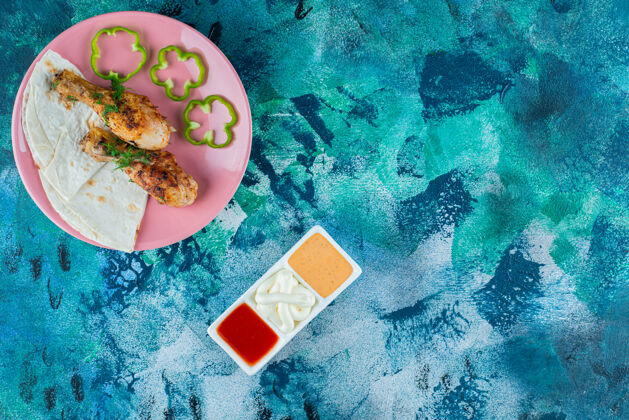 美味在蓝色背景上 将拉瓦什 烤鸡腿和胡椒粉放在酱汁碗旁边的盘子里新鲜蛋白质烹饪