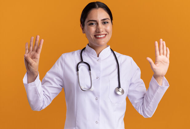 女人年轻的女医生穿着医用外套 脖子上戴着听诊器 面带微笑地看着前面 九号站在橙色的墙上围着秀外套