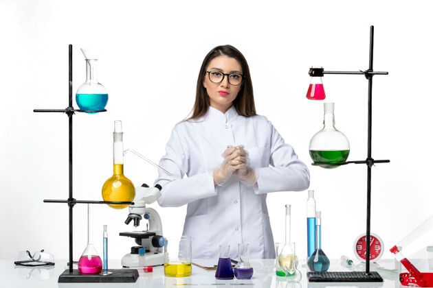 烧杯正面图：穿着无菌医疗服的女化学家站在桌子旁 拿着白色地板病毒疾病疫苗的解决方案-实验室大流行科学医疗罐子实验室