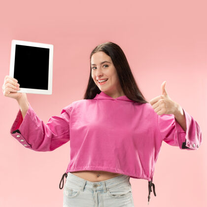 微笑一个自信的休闲女孩的肖像 显示在粉色背景上的笔记本电脑的空白屏幕手持软件个人
