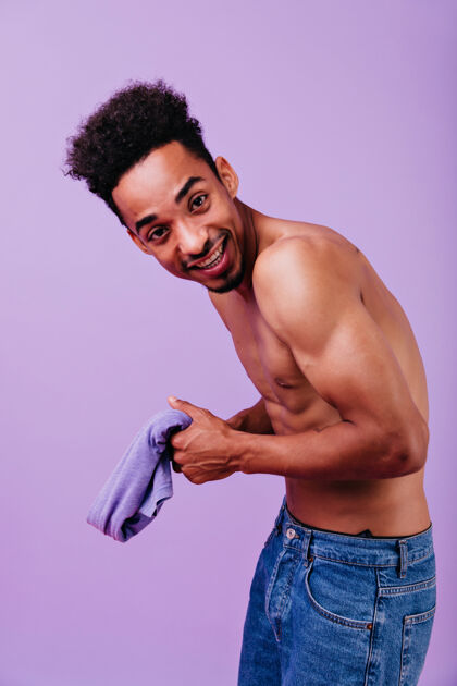 室内一个坚强的微笑的家伙在淡紫色的墙上摆姿势一张没有t恤的感兴趣的非洲男人的室内照片成人时尚家伙