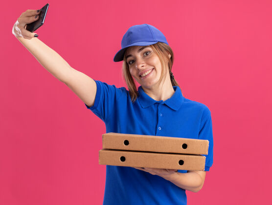 披萨微笑着的年轻漂亮的送货女孩穿着制服拿着比萨饼盒和粉红色的手机盒子年轻电话