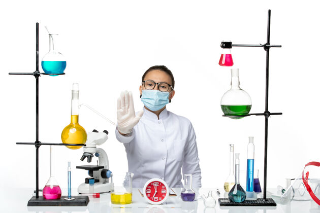 科学前视图穿着白色医疗服的女化学家带着面罩坐在白色背景上的溶液化学家实验室病毒-飞溅前面坐化学家