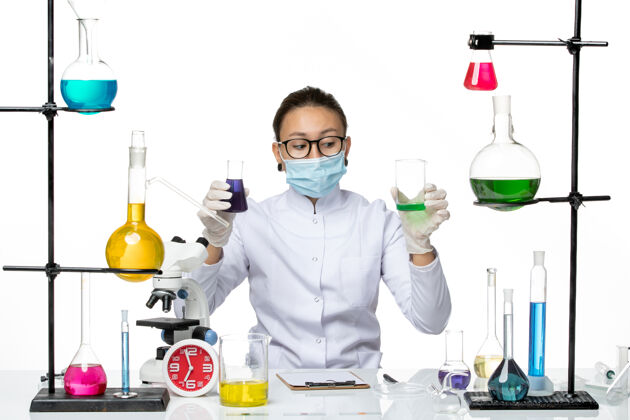 喷溅前视图穿着医疗服的女化学家 戴着面罩 在白色背景上拿着不同的溶液 飞溅着病毒化学实验室的病毒化学面罩前面