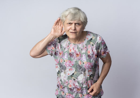 老人困惑的老妇人把手放在耳朵后面 试图听到隔离在白墙上的声音耳朵手女人