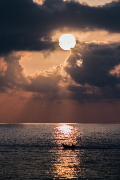热带日落时大海中的船的垂直镜头海岸日出船