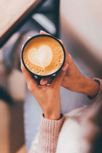 餐馆镜头中的女人手拿一杯热咖啡 用泡沫做成的心形图案桌子特写举行
