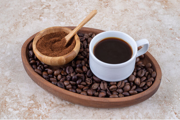 芳香一杯咖啡和一小碗磨碎的咖啡粉放在托盘里的一堆咖啡豆上碗美味粉