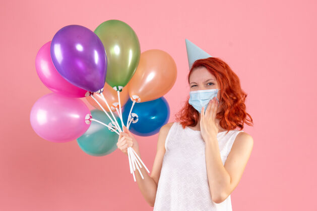 多彩正面图年轻女性手持彩色气球在粉红色的面具上快乐病毒乐趣