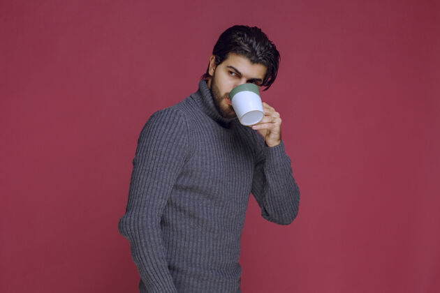 男性穿灰色毛衣的男人从杯子里喝咖啡成人人冬天
