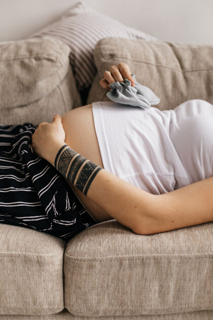 休息有纹身的孕妇拿着小鞋子给宝宝 轻轻地摸肚子腹部感觉年轻