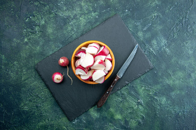 碗上图：整只萝卜和切碎的新鲜萝卜放在碗里 刀放在深色的菜板上 绿黑色混合色背景 有自由空间刀钱包板