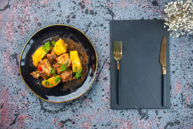 肉美味的晚餐俯视图 黑色盘子里有绿色的土豆肉 餐具放在砧板上 混合颜色背景上有花朵盘子餐具板