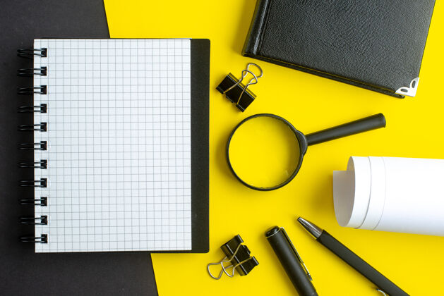 空特写镜头的螺旋笔记本白色空白放大镜笔黑黄混合色背景玻璃电脑笔记本