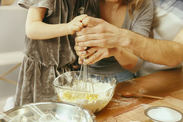 厨房可爱的小女孩和她美丽的父母在家里的厨房里准备蛋糕家庭生活方式的概念晚餐面团微笑