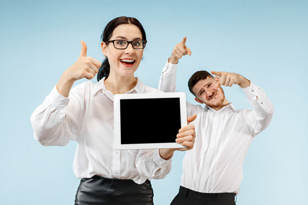 关系在蓝色工作室背景上 惊讶的商务男女微笑着 展示着笔记本电脑或平板电脑的空屏幕男性情感笔记本电脑