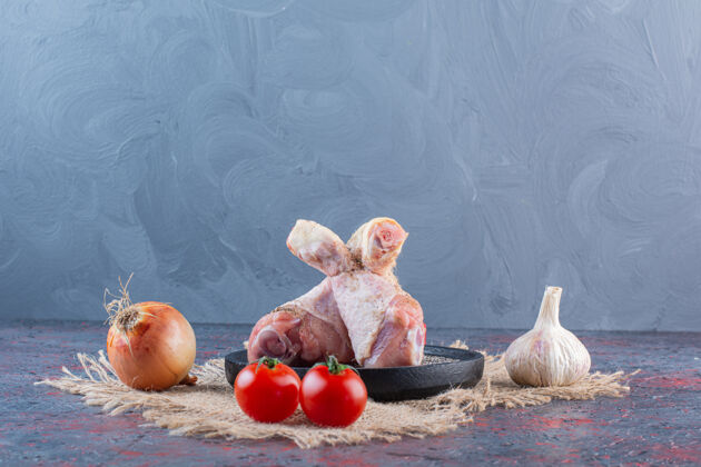 大蒜在大理石表面放着生鸡肉和蔬菜的黑色盘子番茄鸡肉片