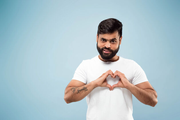 人蓝色背景上穿着白衬衫的印度年轻人的半身特写肖像人类的情感 面部表情 广告概念负面空间展示内心的符号微笑人工作表情