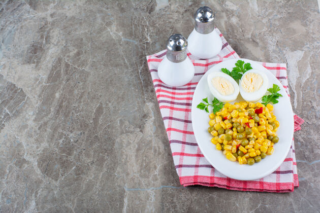 沙拉把玉米沙拉和鸡蛋片放在盘子旁边的盐上 放在茶巾上 放在大理石上好吃的有味道的好吃的